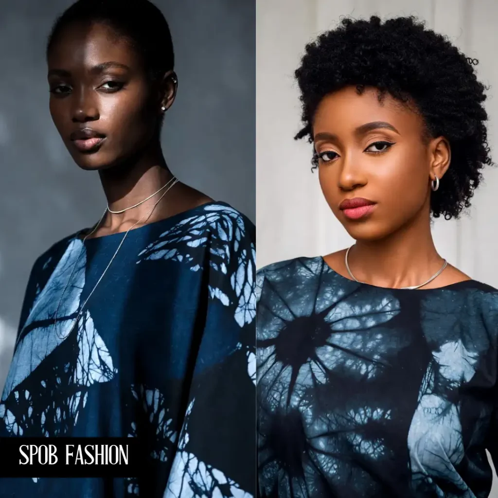 A close-up of a Black woman wearing a shift dress made of "Ghost Adire"—a deep navy fabric with black hand-dyed patterns that are subtle and tonal. She is wearing minimalist silver jewelry. The focus is on the subtle texture of the fabric.